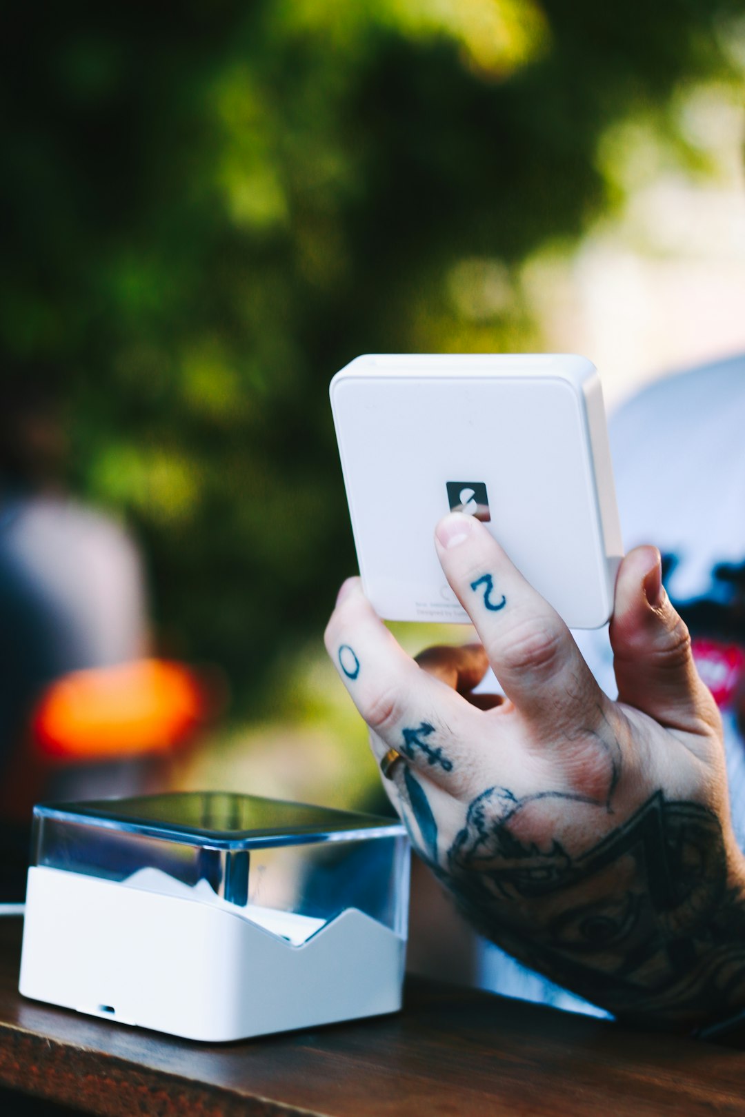 a-tattooed-hand-holding-up-a-white-device-ohxm-098aeg